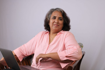 Middle aged Indian woman working on laptop isolated over white background