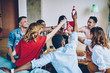 © BullRun - Gesture of cheers during friendly PIZZA party of interracial people in home apartment, happy diverse persons clinking non alcohol beer during weekend time for playing board game in modern flat