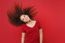 Cheerful Young African American Woman Girl In Casual T-shirt Posing Isolated On Red Background Studio Portrait. People Lifestyle Concept. Mock Up Copy Space. Having Fun, Jumping With Fluttering Hair.