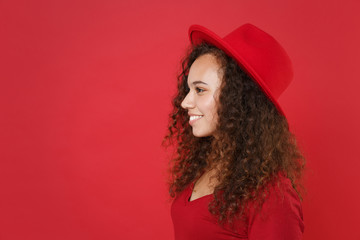 Side view of smiling young african american woman girl in casual t-shirt hat posing isolated on bright red wall background studio portrait. People lifestyle concept. Mock up copy space. Looking aside.