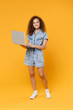 © ViDi Studio - Full length portrait of smiling young african american woman girl in denim clothes isolated on yellow wall background studio portrait. People emotions lifestyle concept. Working on laptop pc computer.