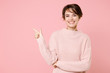 Smiling young brunette woman girl wearing knitted casual sweater posing isolated on pastel pink background studio portrait. People lifestyle concept. Mock up copy space. Pointing index finger aside.