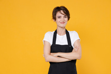 Smiling young female woman 20s barista bartender barman employee in white t-shirt apron work in coffee shop holding hands crossed looking camera isolated on yellow color background studio portrait.