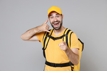 Wall Mural - Delivery employee man guy male 20s in yellow cap t-shirt uniform thermal food bag backpack work courier service during quarantine coronavirus covid-19 virus, posing isolated on gray background studio.