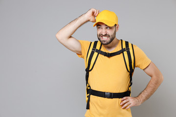 Wall Mural - Delivery employee man guy male 20s in yellow cap t-shirt uniform thermal food bag backpack work courier service during quarantine coronavirus covid-19 virus, posing isolated on gray background studio.