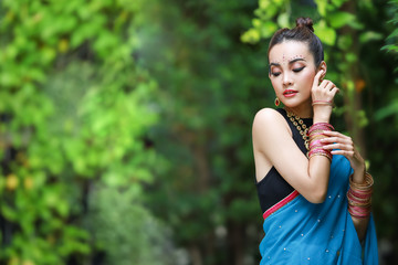 Portrait of beautiful young asian Thai girl.  Woman model with kundan jewelry set and traditional hindu India costume blue saree and lehenga dress in garden.