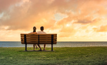 Couple Sitting On Park Bench Watching The Sunset. Love And Relationships Concept. 
