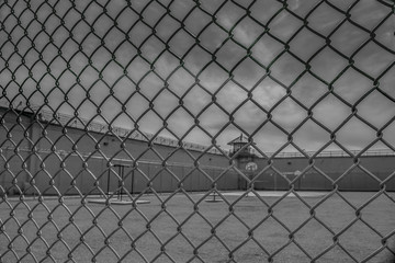 View of the exercise yard at Kingston Penitentiary with exercise equipment, guard tower, walls and barbed wire through chain link fence nobody