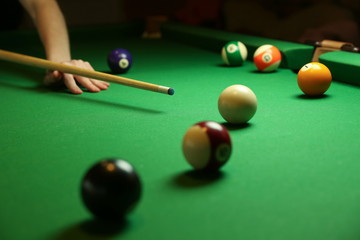 Wall Mural - pool balls and billiard cue on green billiard table. the hand of a billiard player holds a cue on a pool table. billiard player strikes a white ball