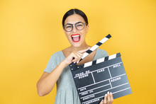 Young Beautiful Woman Wearing Glasses Standing Over Isolated Yellow Background Holding Clapperboard Very Happy