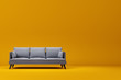 Grey couch with pillows on studio yellow background.
