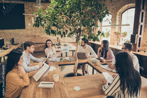 Fototapeta na drzwi i meble Photo of business people partners sit around table spacious office seven members successful new anti crisis crash plan professionals discussing observe graphics charts 2020 ending indoors