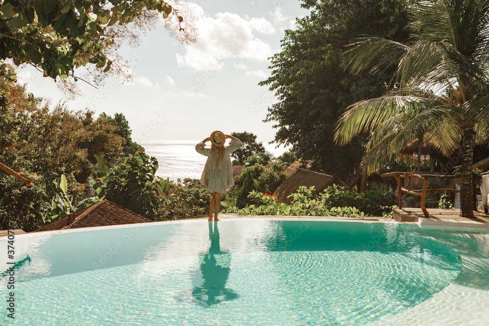 Back view girl in straw hat standing on the edge of infinity pull and ...