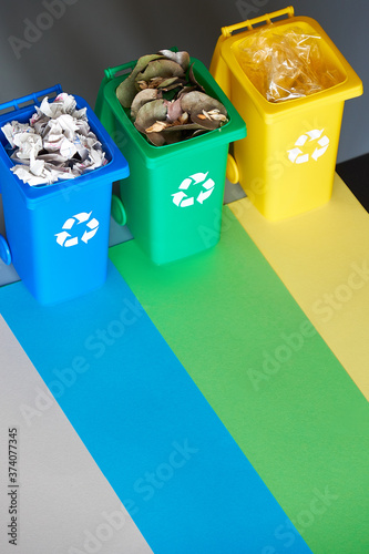 Three color coded recycle bins, isometric picture on geometric paper background with copy-space. Recycling sign on the bins - blue, yellow and green. Waste separation concept.