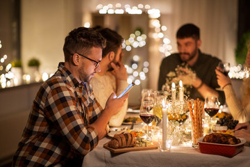 Wall Mural - holidays and people concept - man with smartphone at dinner party with friends at home