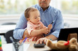 © Syda Productions - remote job, multi-tasking and family concept - middle-aged father with baby, calculator and tablet computer working at home office