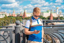 A Young Blond Man Calls On A Mobile Phone With A View Of The Kremlin And The River In Moscow