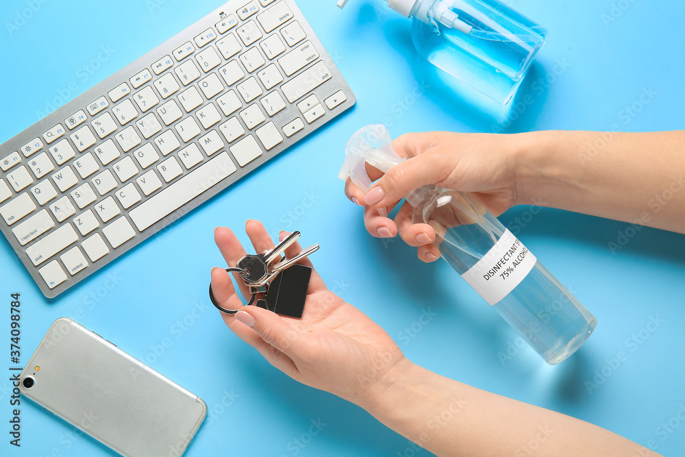 Woman disinfecting keys from house on color background