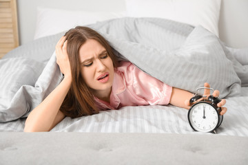 Wall Mural - Young woman with alarm clock suffering from insomnia in bedroom