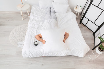 Canvas Print - Young man with alarm clock suffering from insomnia in bedroom