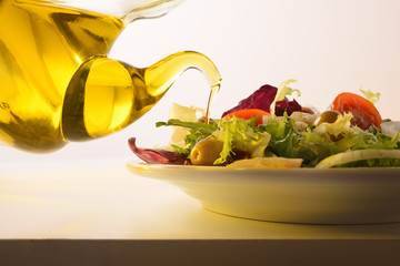 Pouring olive oil from oil dispenser on salad white table