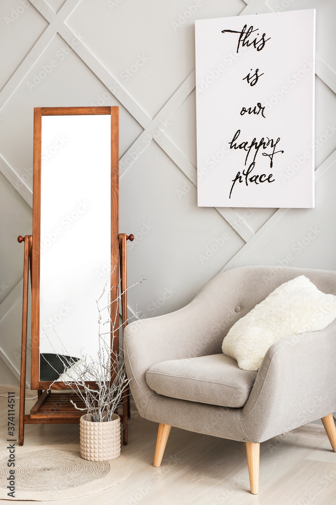 Big mirror with armchair near grey wall in room