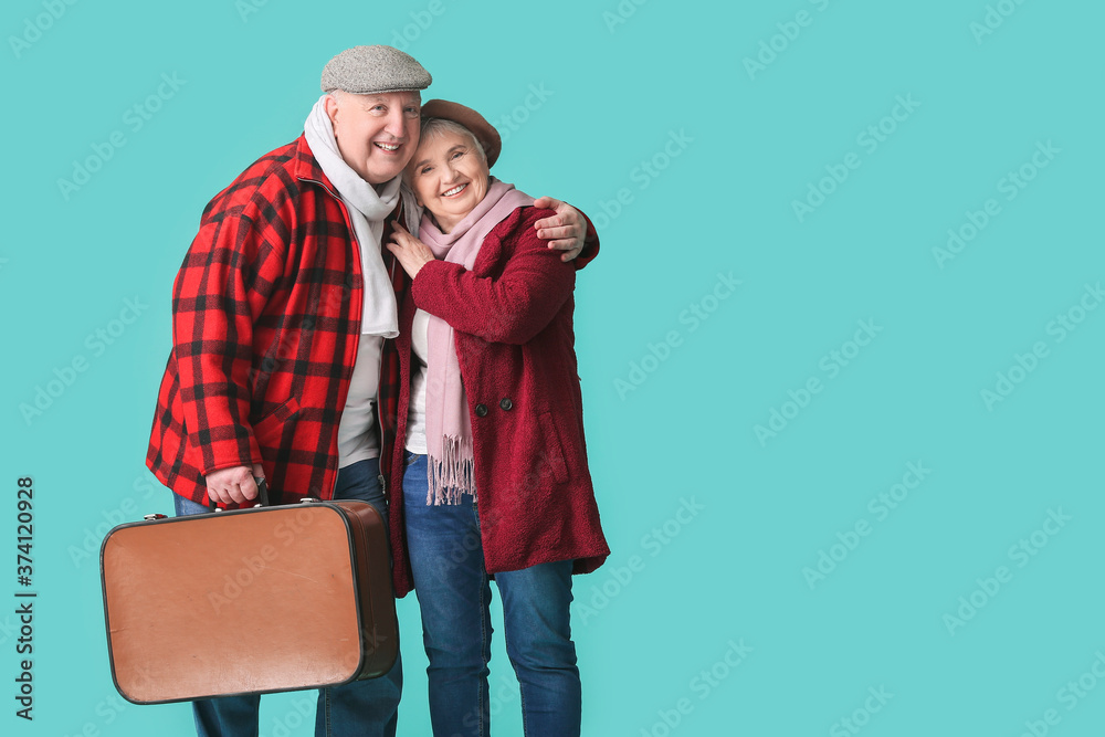 Happy senior couple with packed suitcase on color background