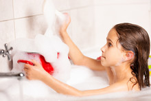 Cheerful Little Caucasian Girl Plays With Foam While Bathing In The Bathtub