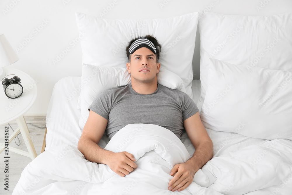 Young man suffering from insomnia in bedroom