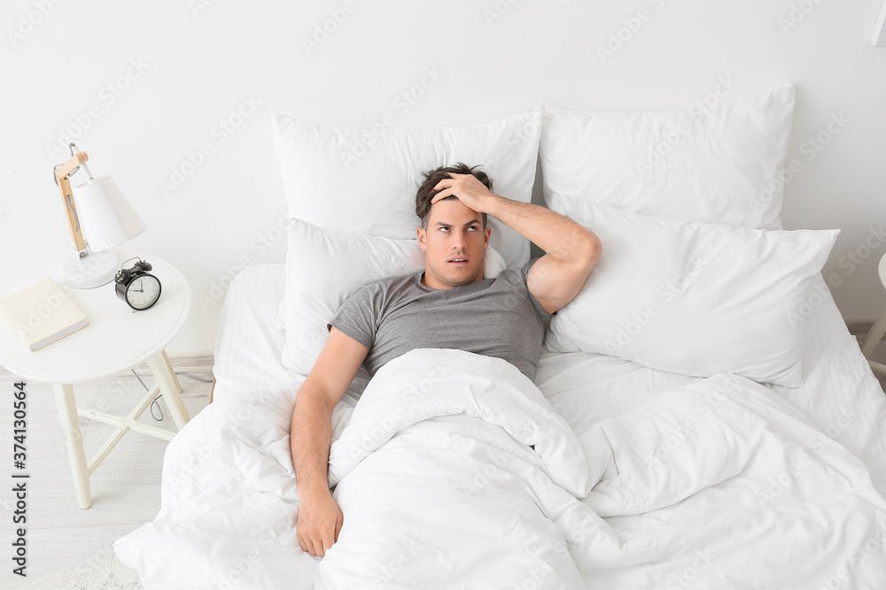Young man suffering from insomnia in bedroom