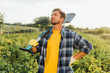 © LIGHTFIELD STUDIOS - rancher in checkered shirt looking away while standing with hand on hip with shovel in field