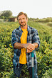 © LIGHTFIELD STUDIOS - farmer in plaid shirt looking at camera while standing with shovel in field