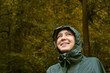 © karinabost - Portrait of happy smiling woman wearing waterproof raincoat with hood in rainy autumn day. Woman is walking in the forest, looking up