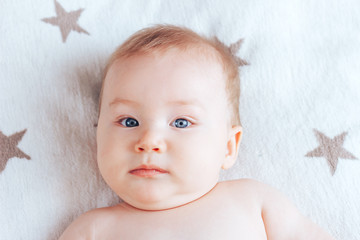 Wall Mural - A photo of an emotionless baby, a newborn baby with blue eyes and blond hair lying on a light blanket with brown stars