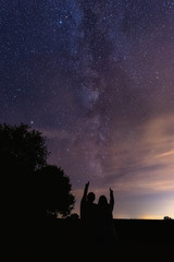 Wall Mural - Vertical shot of silhouettes of a couple pointing at the milky way in the night sky