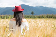 © Fernanda - Young woman standing in the middle of a golden wheat field enjoying the sunset - girl with red hat in a field surrounded by mountains - woman alone in the field