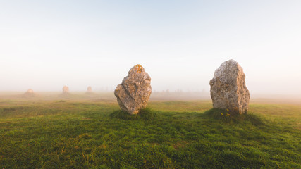 Menhir alignment view at Camaret sur mer in a morning fog at sunrise. Brittany, France. Golden sunlight. Picturesque scenery. Travel destinations, national landmarks. sightseeing, history, culture