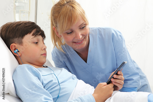 Cuadros en Lienzo Sick child lying in bed in hospital room and smiling nurse using smartphone surf