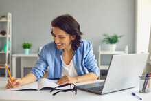 Smiling Woman Making Notes During Online Lesson Or Meeting On Laptop
