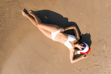 Wall Mural - Young woman wearing Santa hat and bikini on sunny beach, top view. Christmas vacation