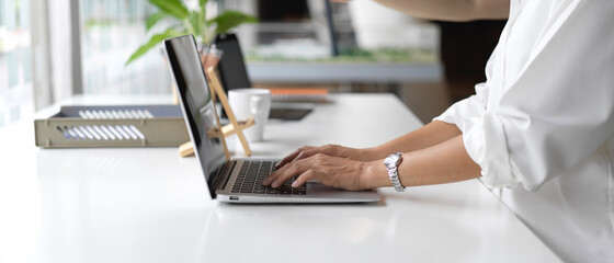 Side view of female hands typing on laptop keyboard on worktable