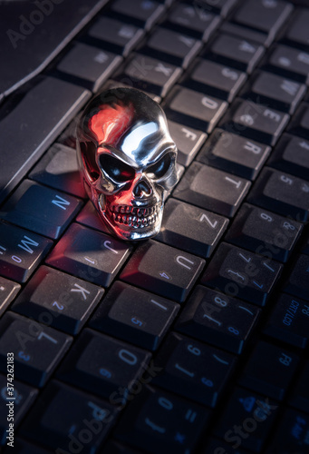A skull made of shiny metal lies on a keyboard of a computer with strong red reflections