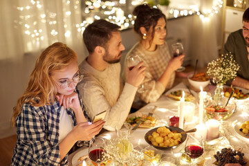 Wall Mural - holidays, technology and people concept - young redhead woman in glasses with smartphone at christmas dinner party with friends at home