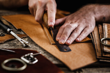 Wall Mural - Close up of a shoemaker or artisan worker hands. Leather craft tools on old wood table. Leather craft workshop.