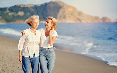 outdoor portrait of smiling happy caucasian senior mother with her adult daughter hugging and walkin