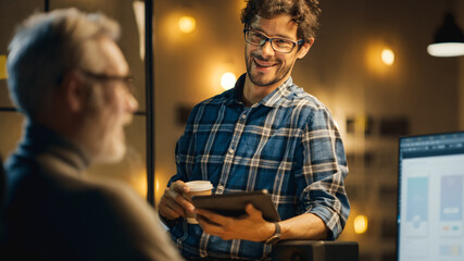 Poster - In the Evening Creative Middle Aged Smartphone Software Developer Works on a Desktop Computer with Screen Showing Application Design, Has Conversation with Younger Specialist who Uses Tablet Computer