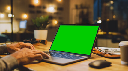 Close-up On the Hands of the Male Specialist Works on a Laptop Computer with Mock-up Green Screen. In the Background Evening in the Stylish Studio Office