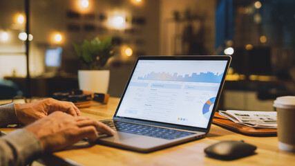 Poster - Close-up On the Hands of the Male Specialist Works on a Laptop Computer, Screen Shows Various Data and Statistics. In the Background Evening in the Stylish Studio Office