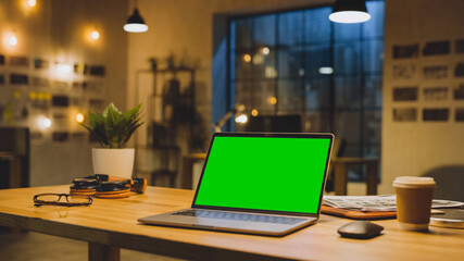 Wall Mural - Mock-up Green Screen Stanting on the Desktop. In the Background Stylish Modern Office Studio in the Evening with Big Cityscape Window