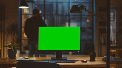 Aufkleber - Desktop Computer with Mock-up Green Screen Standing on the Desk in the Modern Creative Office. In the Background Designer Drinks from a Cup Looks at the Night City out of the Window.